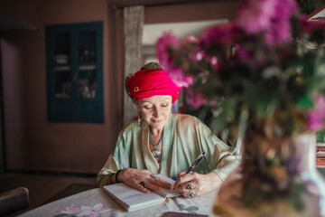 Woman with a turban on her head writes a letter sitting in her living room