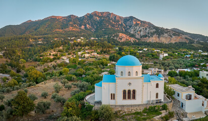Naklejka premium Aerial, panoramic view of the Lagoudi Zia Church on Greek island of Kos. Typical blue roofs monastery near Zia town against mountains in background. Sunset colors, no people, calm atmosphere.