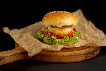 Close-up of a delicious fresh homemade burger with lettuce, cheese, onion and tomato on a rustic wooden board on a dark background