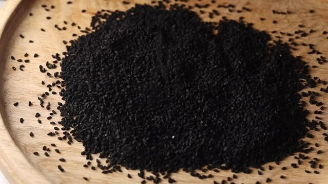 black cumin seeds on a wooden plate slow motion Sprinkle the seeds on a plate. 