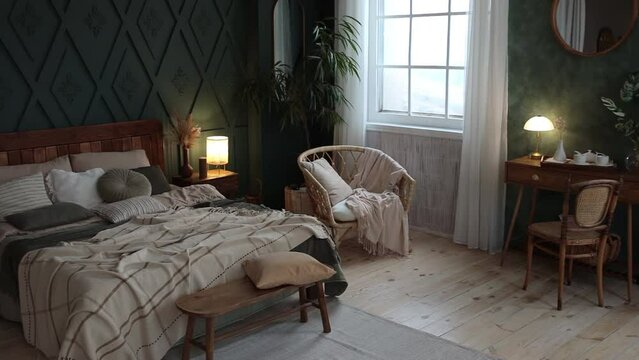 Cozy spacious bedroom interior in boho style with green walls, wooden furniture, console table, textiles, large windows and potted plants. Empty space