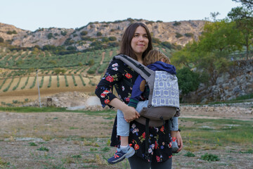 young mother carrying her child in a backpack baby carrier
