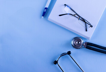 Doctor's set: a notebook for recording patient complaints, a pen, a fanendoscope, glasses and tablets and vitamins. Medical background. Medical first aid kit and medicine concept.