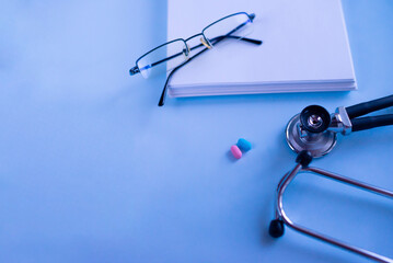 Doctor's set: a notebook for recording patient complaints, a fanendoscope, glasses and pills and vitamins. Medical background. Medical first aid kit and medicine concept.