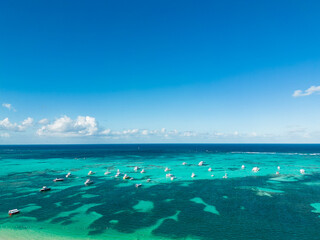 Aerial view of many anchoring yachts and tourist boats in the turquoise Caribbean sea. Clear blue sky on the horizon. Best destination for vacation in Punta Cana