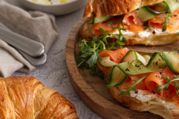 Croissants with cheese cream, red fish and cucumber on a wooden stand served for breakfast or lunch