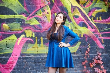 Portrait of a girl in a bright blue dress against a wall with graffiti. Autumn leaves.