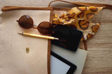 Retro bag with book, tablet, phone, pen, glasses and leopard pattern scarf. Top view, wooden background.