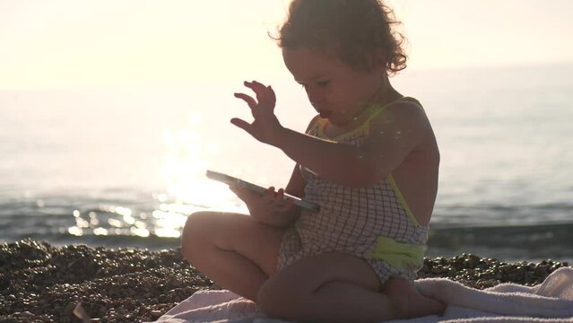 Baby girl uses smartphone on the beach