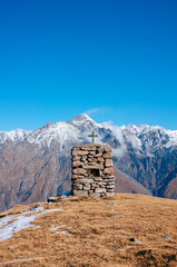 the summit cross in the mountains of Georgia. In the foreground a hill with yellow grass, behind it...