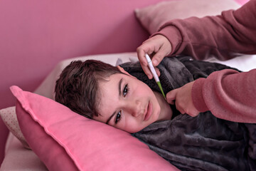 Sick boy with thermometer laying in bed and mother hand taking temperature. Mother checking...