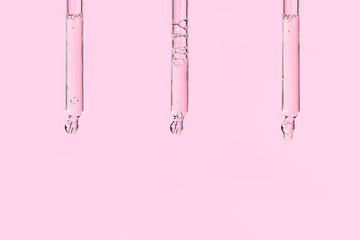 Three glass pipettes with facial serum on light pink background. Liquid gel or essential oil with...