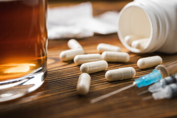 White pills, syringe with a drugs dose, narcotics, glass with alcohol drink on a wooden table,...