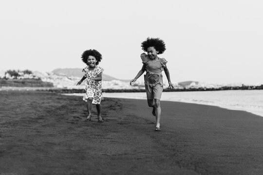 Happy african sister twins running on the beach together during summer time - Main focus on right girl hands - Black and white editing
