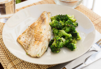 fried fillet of sea bass with garnish of broccoli on black warm stone plate