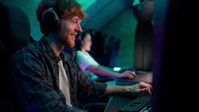 Friendly ginger man gamer in headphones playing RPG video game on a championship. Stylish Neon Cyber Games