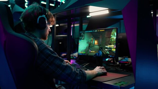 Concentrated ginger man gamer in headphones playing RPG video game on a championship. Stylish Neon Cyber Games