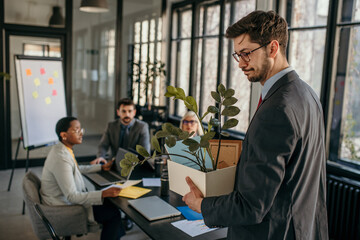 Sad businessman getting fired and leaving office with his belongings during a meeting.