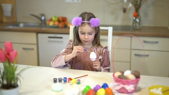 The girl paints decorative eggs for Easter. Colorful eggs in a basket.