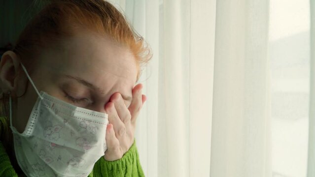 The girl in the mask is sick and longingly looks out the window into the street. Flu and fever.