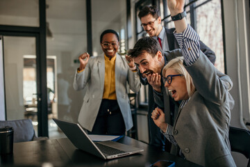 Obraz premium Shot of diverse business people working together on laptop. Creative female and male executives celebrating great business news.