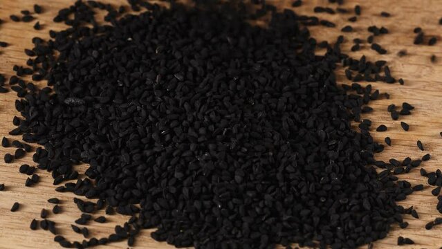 Black cumin seeds poured on a wooden board, macro 