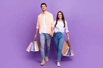 Full size photo of two cheerful lovely partners hold hands walking boutique bags isolated on violet...
