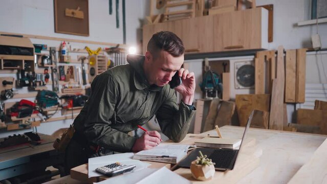 Carpenter talking to a furniture customer on the phone in his own workshop