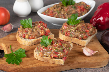 Homemade eggplant caviar with pepper, tomato and garlic on bread toasts on wooden board