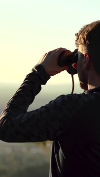 Man looking at the horizon using binoculars in the mountain. Sunset time