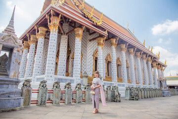 Young woman wearing Thai dress with accessories holding a bag at Wat Arun Ratchawararam It is a...