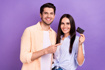 Photo of positive cheerful husband wife dressed shirts pointing finger credit card isolated purple color background