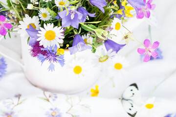 Bouquet of beautiful meadow flowers  in white vase on embroidered tablecloth on white background indoors in natural light, still life with vivid wild colorful flowers, close up view