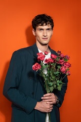 Portrait of smiling man in blue jacket holding roses on red background.