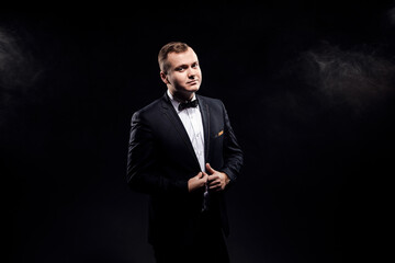 Handsome confident businessman wearing suit with bow tie standing isolated over black background