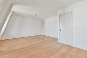 an empty room with white walls and wood flooring on the right, there is a door leading to another...