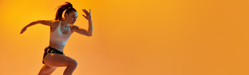 Dynamic image of young sportive girl, professional runner training over orange studio background in neon light. Concept of sportive lifestyle, health, endurance, motion. Banner. Copy space for ad