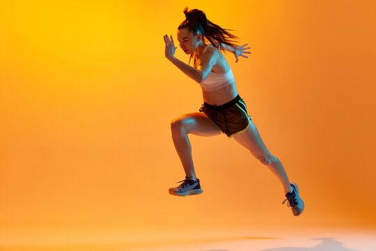 Running. Dynamic image of professional female runner, athlete training over orange studio background in neon light. Concept of sportive lifestyle, health, endurance, action and motion. Ad