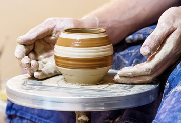 Male hand with clay pot with pattern on a pottery wheel
