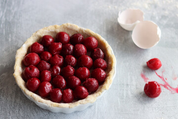 Homemade sweet cherry pie in a making. Close up photo of fruit tart on light grey table. 