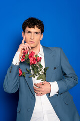 Stylish model in shirt and jacket holding flowers and posing on blue background.