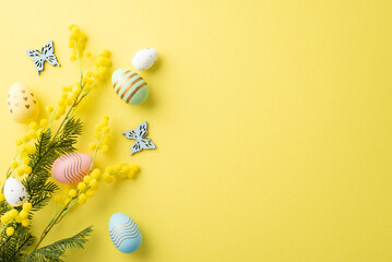 Easter decor concept. Top view photo of colorful easter eggs bouquet of mimosa flowers and butterflies on isolated yellow background with copyspace