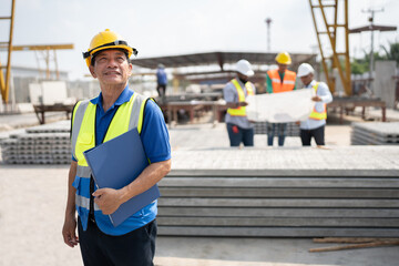 Portrait Asia senior engineer man holding document file with team working with paper work and precast cement factory background	