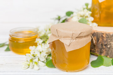 Sweet honey jar surrounded spring acacia blossoms. Honey flows from a spoon in a jar. jars of clear...