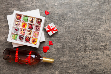 Bottle of red wine on colored background for Valentine Day with gift and chocolate. Heart shaped with gift box of chocolates top view with copy space