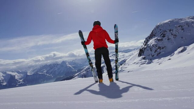 Skier posing on winter mountains with skis and looking at the valley. Beautiful scenery with freshly groomed ski slope.