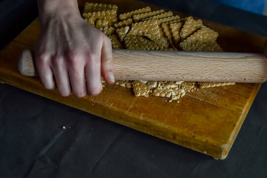 hands that break biscuits with a rolling pin to prepare the crunchy base of a cheesecake