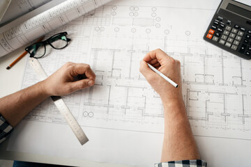 close up of hand professional architect, engineer or interior reviewing blueprint on workplace desk in office center at construction site