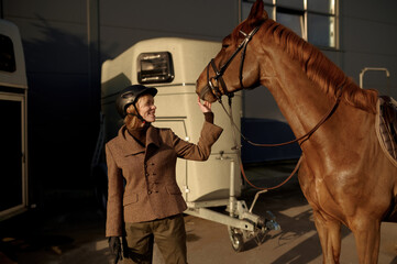 Young adult smiling rider woman stroking horse nose