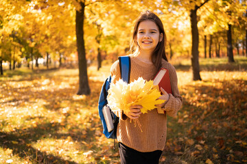 Back to school. Adorable girl with school backpack and book having fun with yellow maple leaves in...